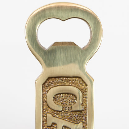 A close-up of a solid brass bottle opener with 'Captain' written on it. Photographed on a white background.