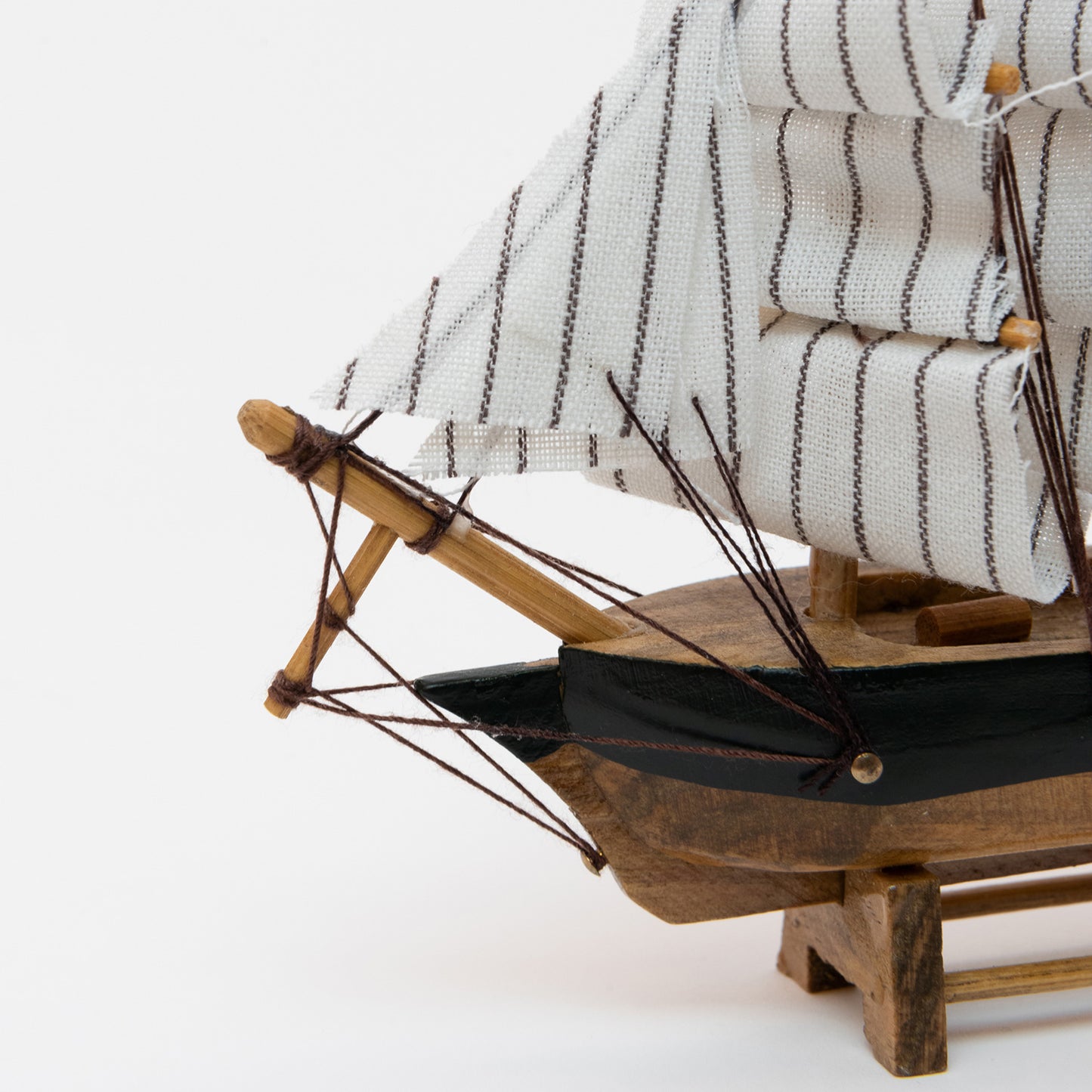 Close-up view of the model clipper's bow with wooden hull and white stripy sails.