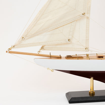 Close-up view of the model Colombia Yacht's bow with white and burgundy hull and cream coloured sails.