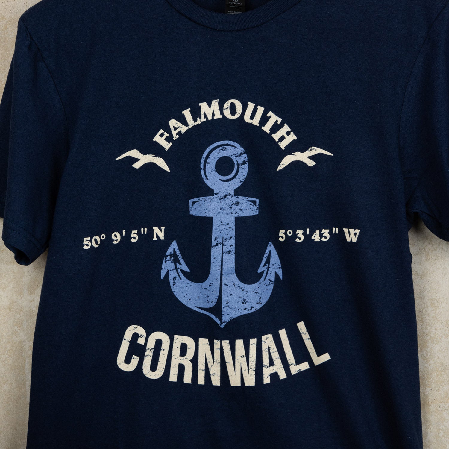 Close up of navy blue cotton t-shirt with bespoke design featuring the wording Falmouth, Cornwall around a distressed blue anchor.