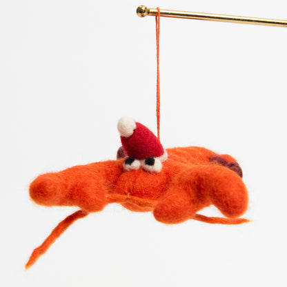 A Christmas lobster decoration hanging on a metal rod. The decoration is an orange felt lobster wearing a red Christmas hat.