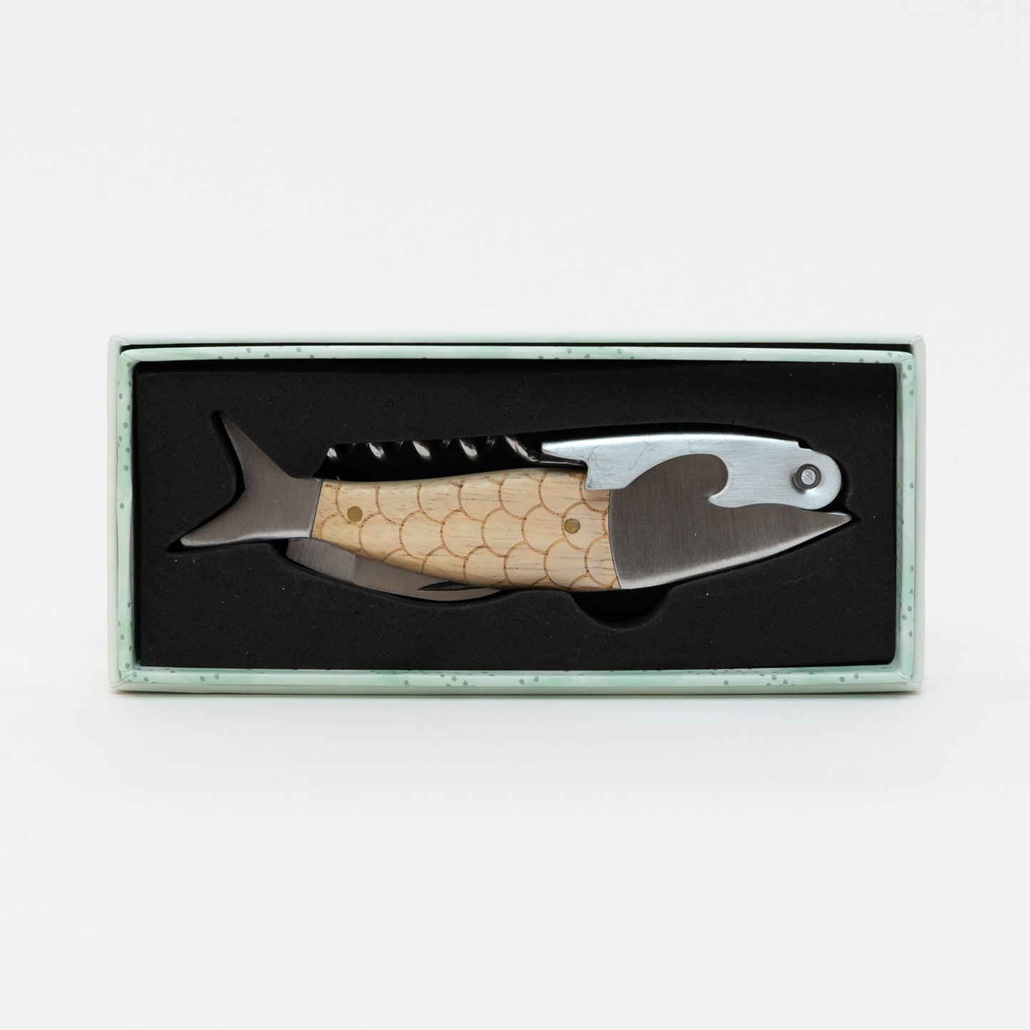 Top down view of the metal and wood fish bottle opener in its box.