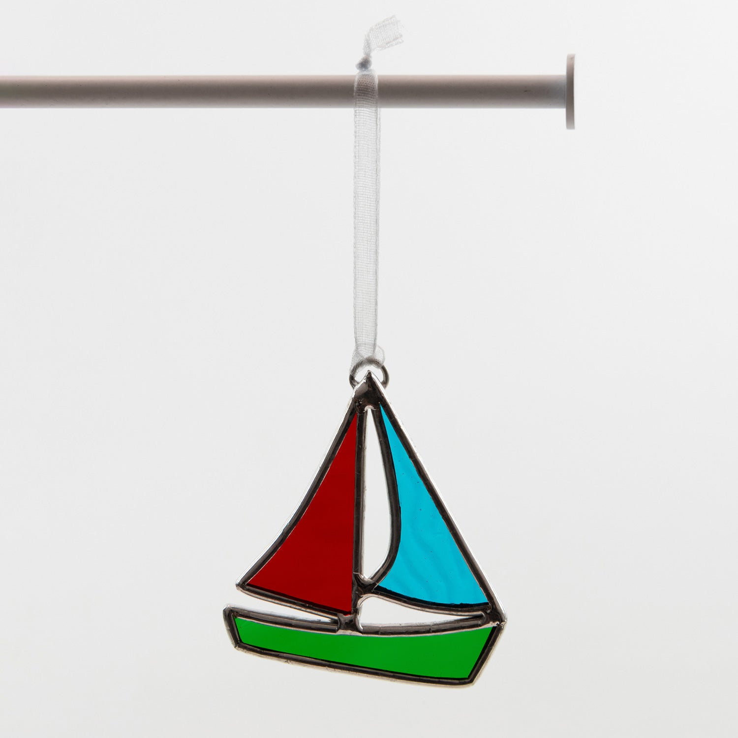 Glass sailboat decoration hanging from a light grey ribbon. This sailboat is made from red, green and blue glass.