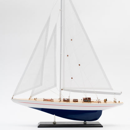 Side view of the Model J Class Yacht with white sails and a blue and white hull.