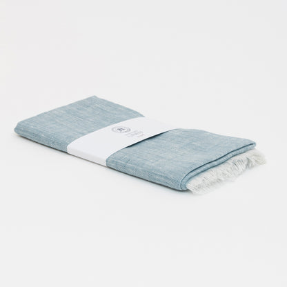 A photo of the sea blue linen scarf packaged on a white background.