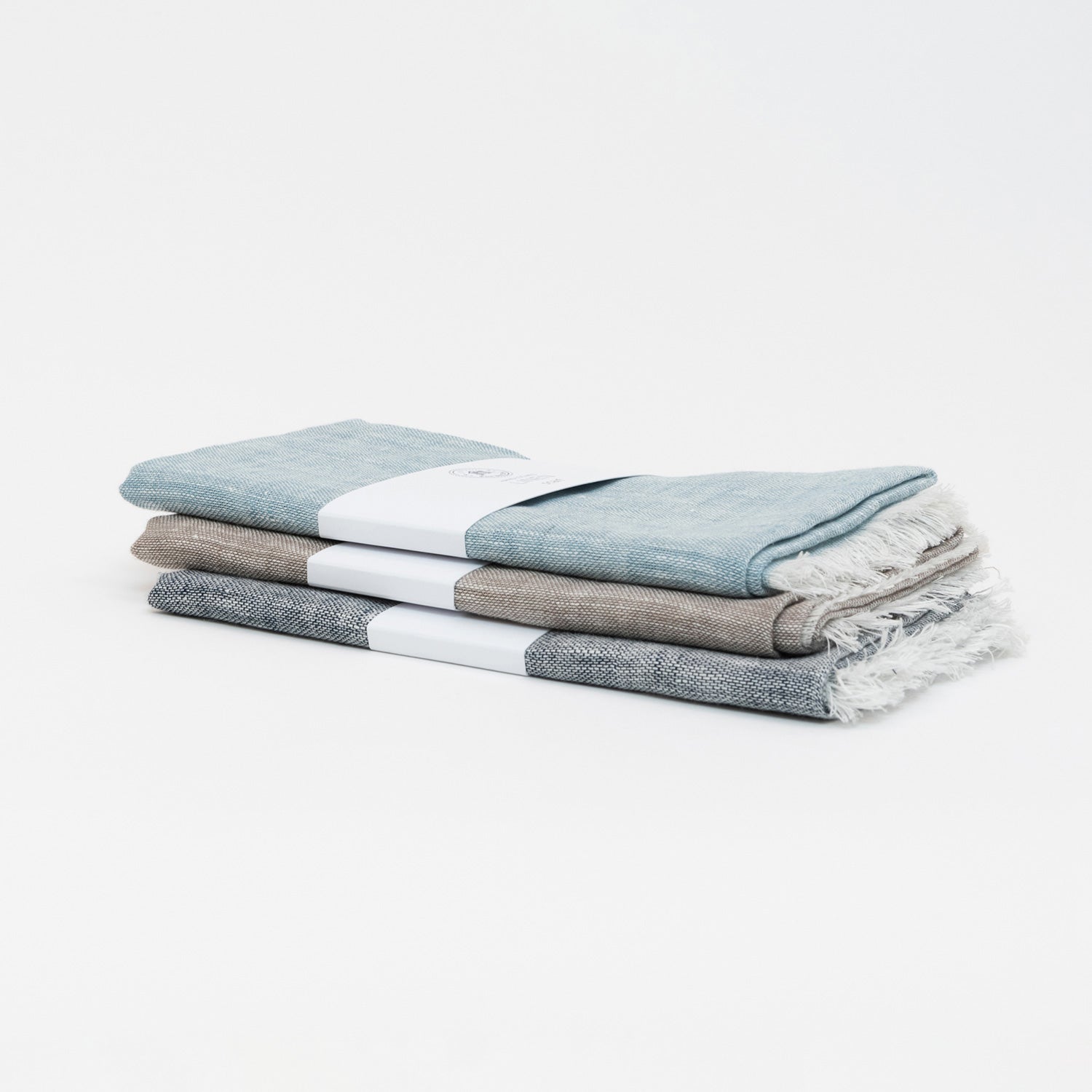 Three linen scarf colour variants piled on top of each other. Denim blue, sand, and sea blue.