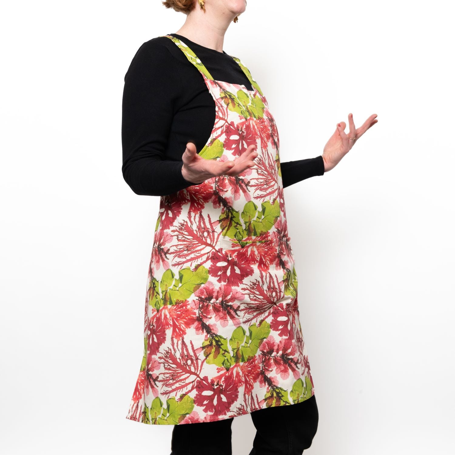 side shot of Model wearing a cross back apron in green and pink coloured seaweed design