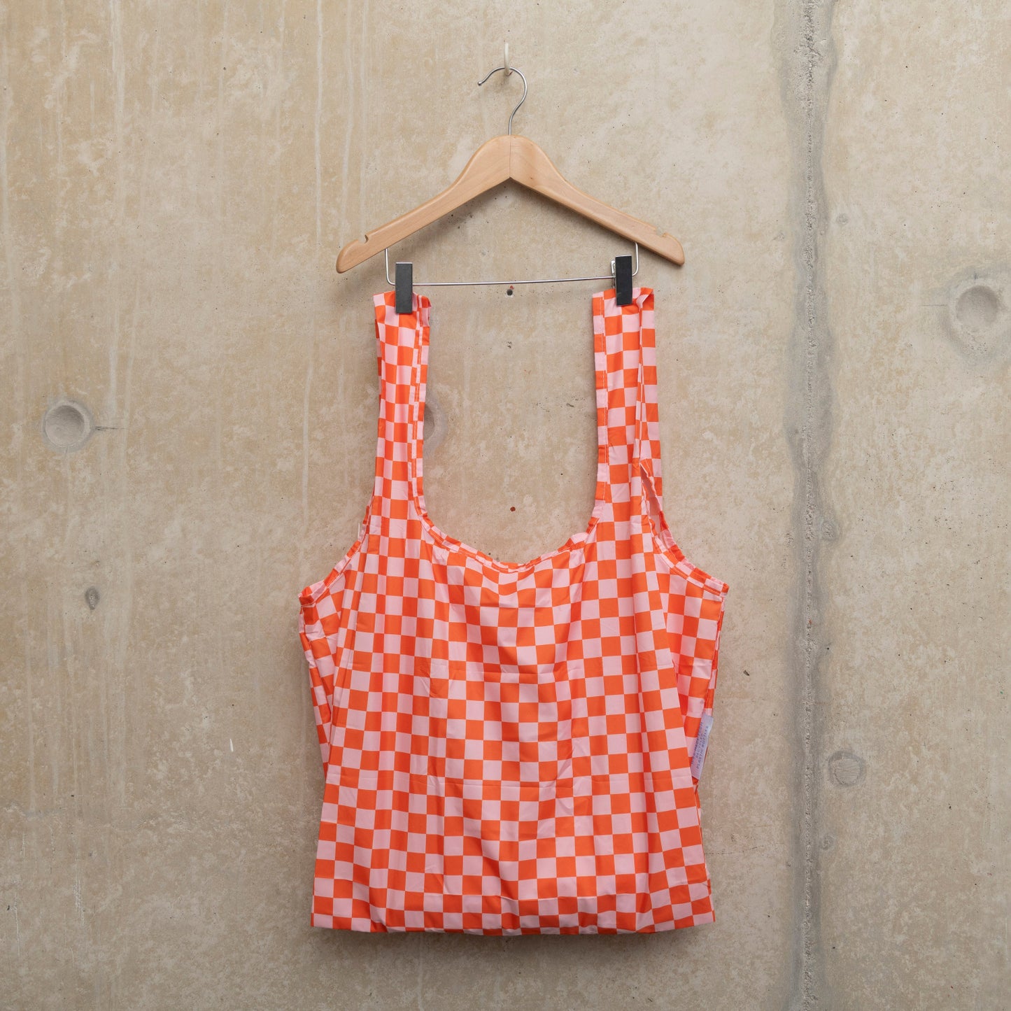 Image of checkerboard design bag in pink and orange, hanging on a wooden hanger against a concrete wall.