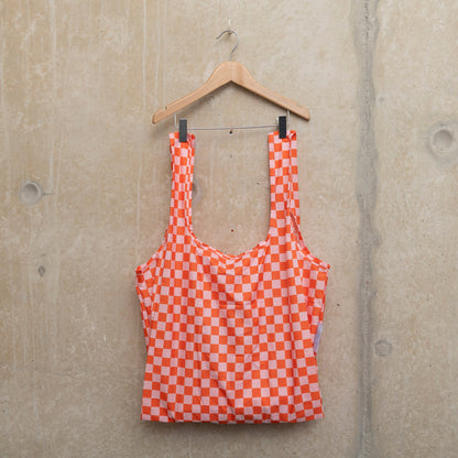 Image of checkerboard design bag in pink and orange, hanging on a wooden hanger against a concrete wall.