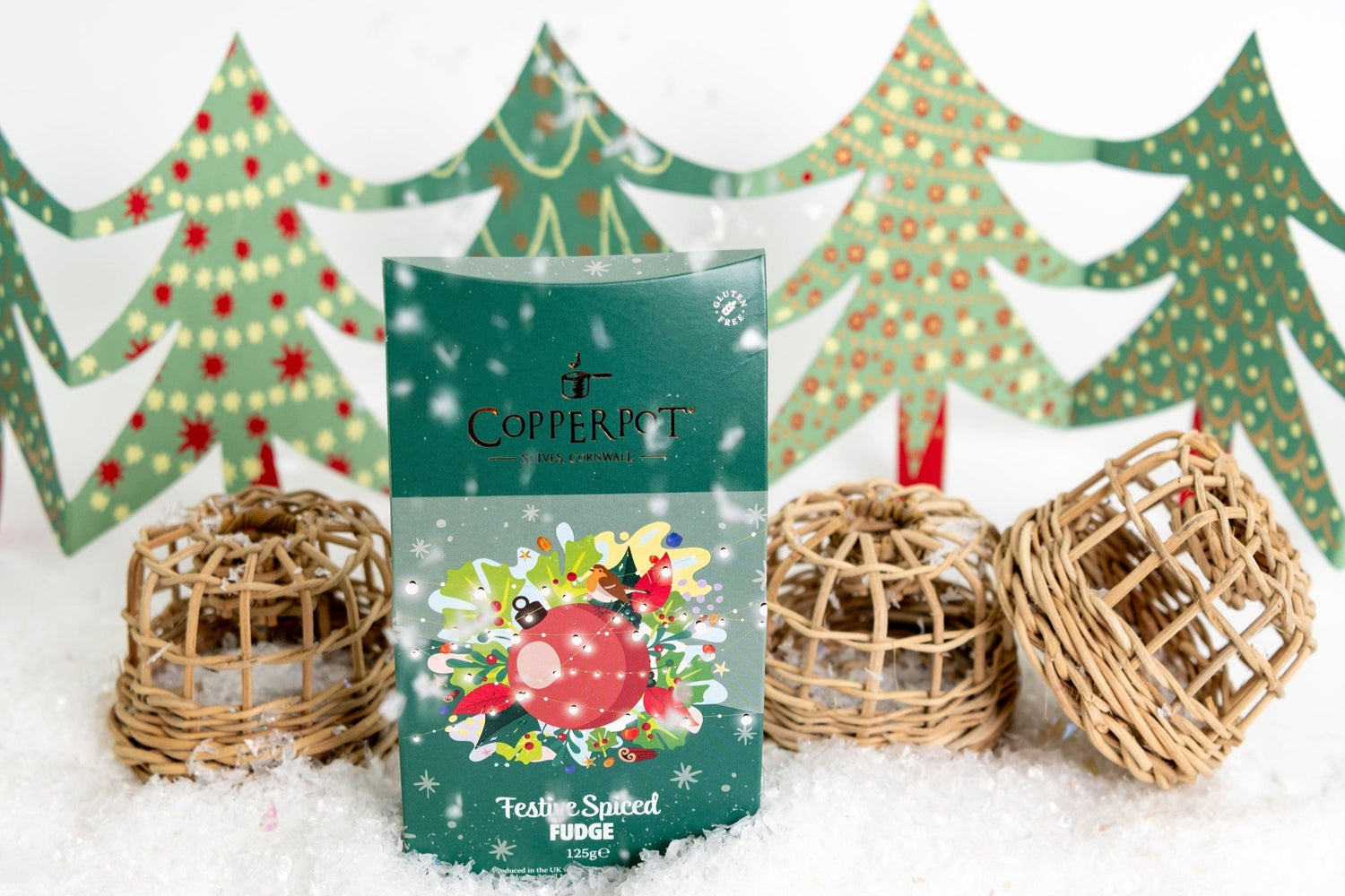 A photograph of a Festive Fudge product with a snowy foreground and a background of decorated paper Christmas trees and miniature lobster pots.