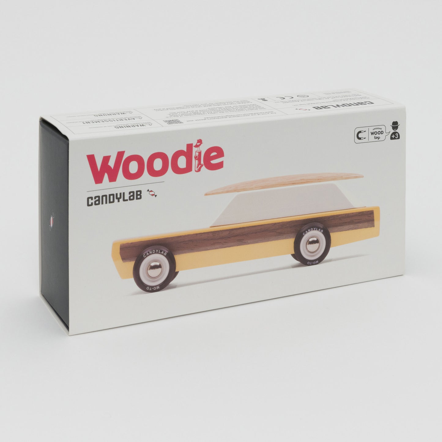 A photograph showing a yellow wooden toy car with wooden surfboard on its roof.