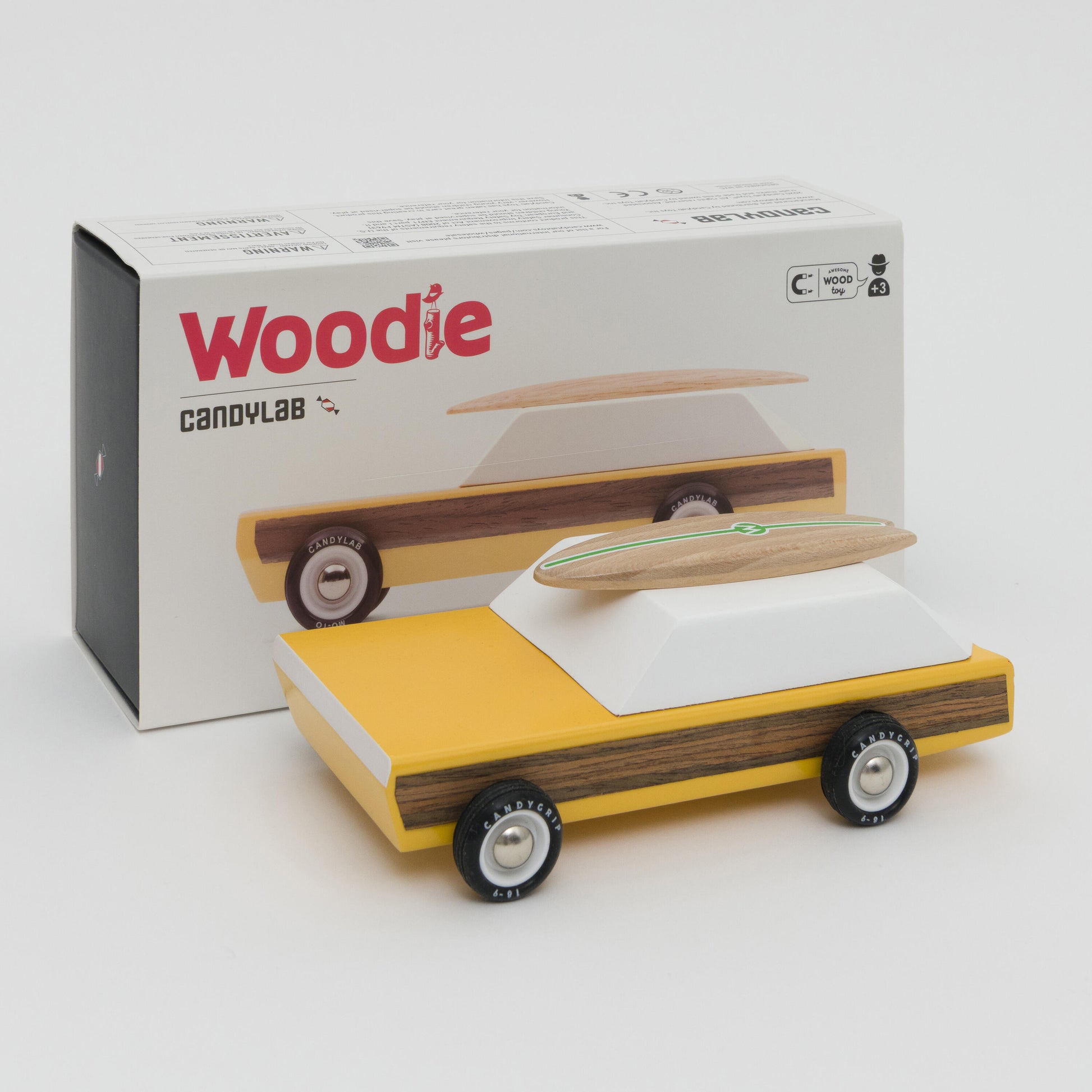 A photograph showing a yellow wooden toy car with wooden surfboard on its roof.