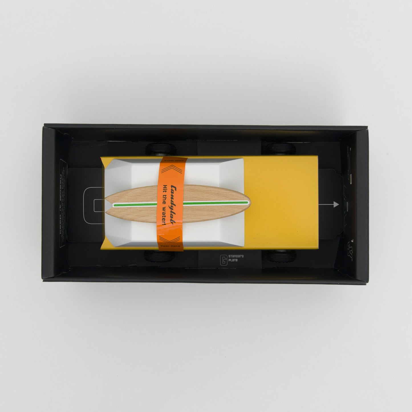 A photograph taken from above showing a yellow wooden toy car with wooden surfboard on its roof.