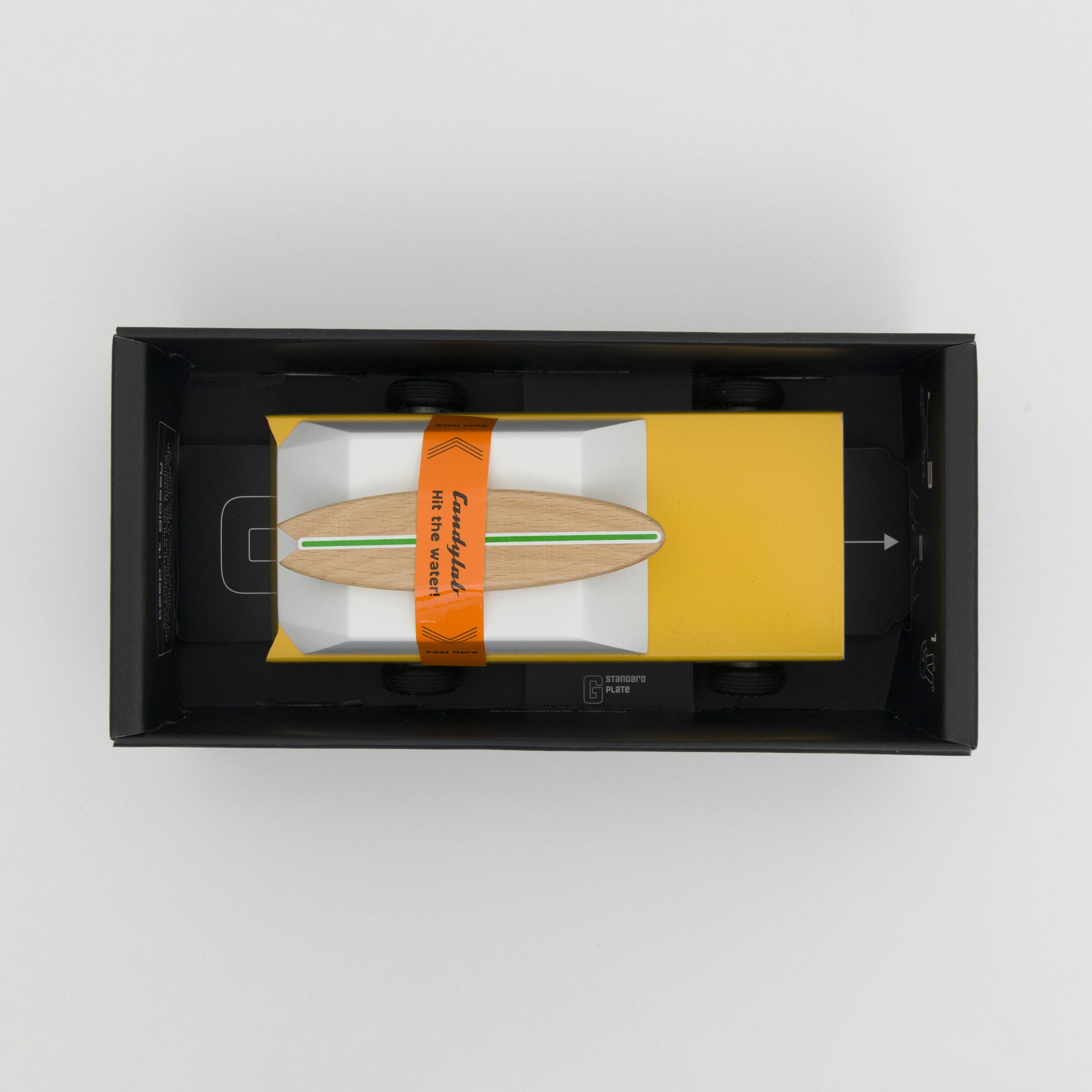 A photograph taken from above showing a yellow wooden toy car with wooden surfboard on its roof.