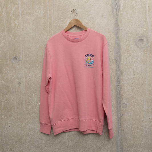 Bright pink sweatshirt with small surf motif on left chest. Motif shows round character surfing a wave with the wording SURF! Falmouth, Cornwall.