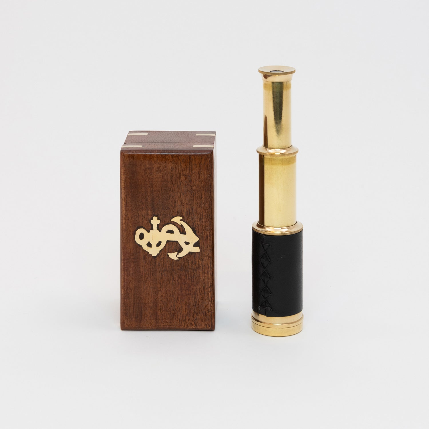A photo of a brass pocket telescope next to a wooden box. Pictured on a white background.