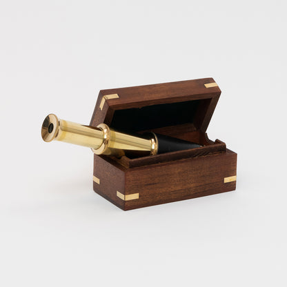 A photo of a brass pocket telescope inside a wooden box. Pictured on a white background.