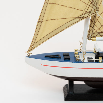 A close-up view of the bow of the model racing yacht with a black and white hull, brass details and tan sails.