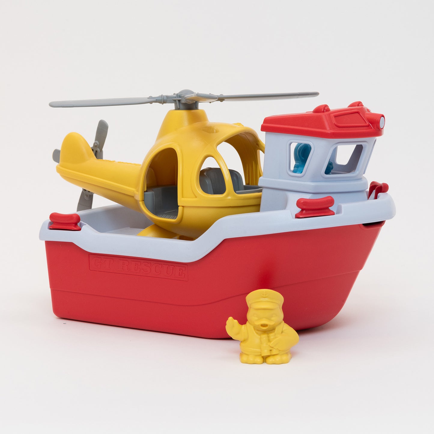 A red and white toy boat with a yellow helicopter on the deck and a small yellow toy penguin captain.