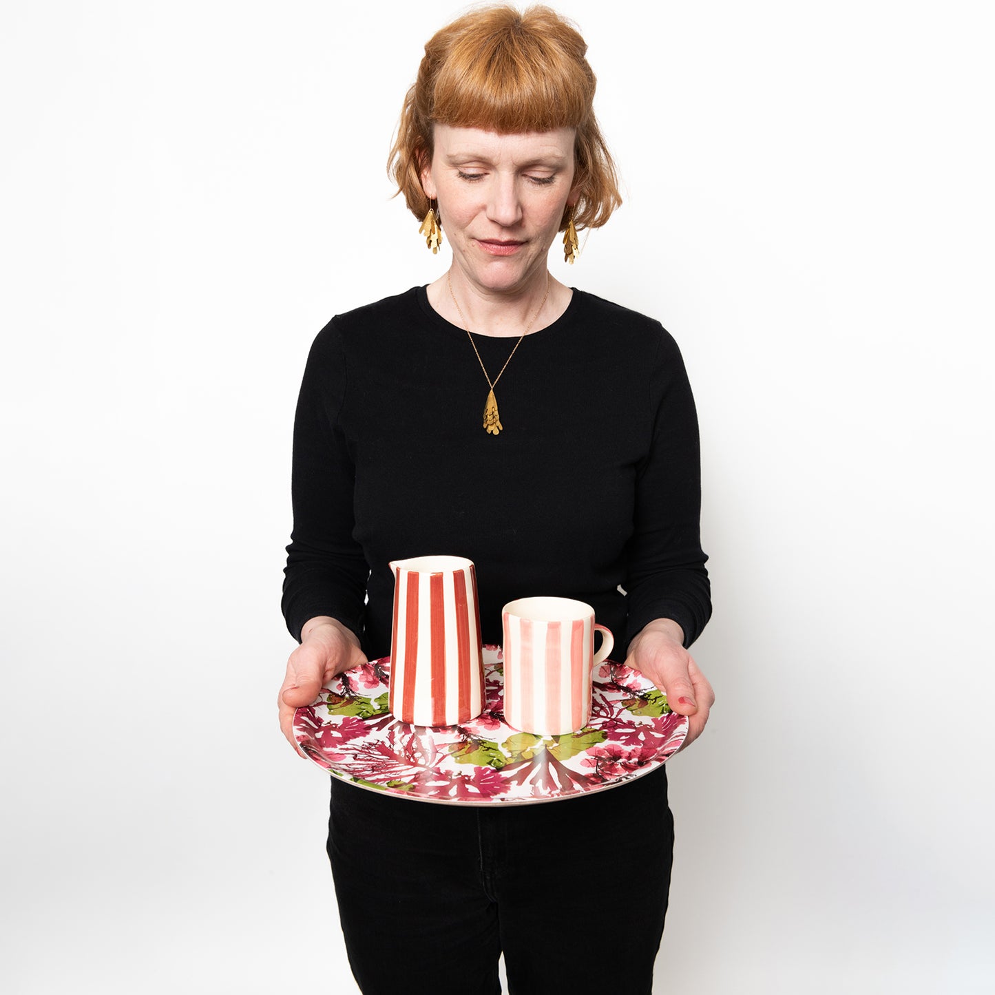 Model holing the round tray with a jug and a mug on the tray to show size