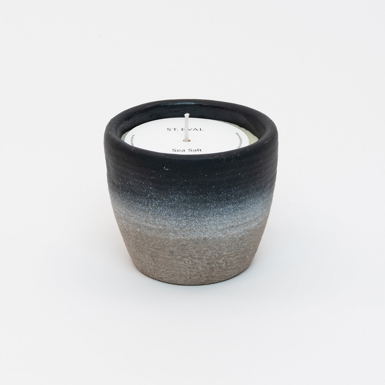 St Eval Sea Salt Small Coastal Candle in heavy stoneware pot. Natural stone clay base fading into a deep navy blue ring at top of pot. St Eval card circle protector on top of candle with wick standing tall.