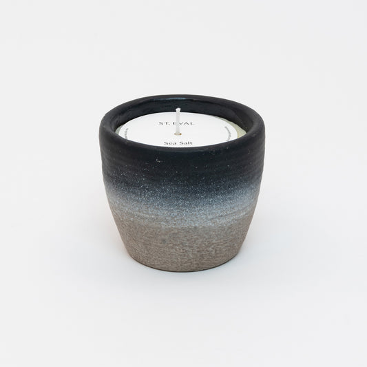 St Eval Sea Salt Small Coastal Candle in heavy stoneware pot. Natural stone clay base fading into a deep navy blue ring at top of pot. St Eval card circle protector on top of candle with wick standing tall.