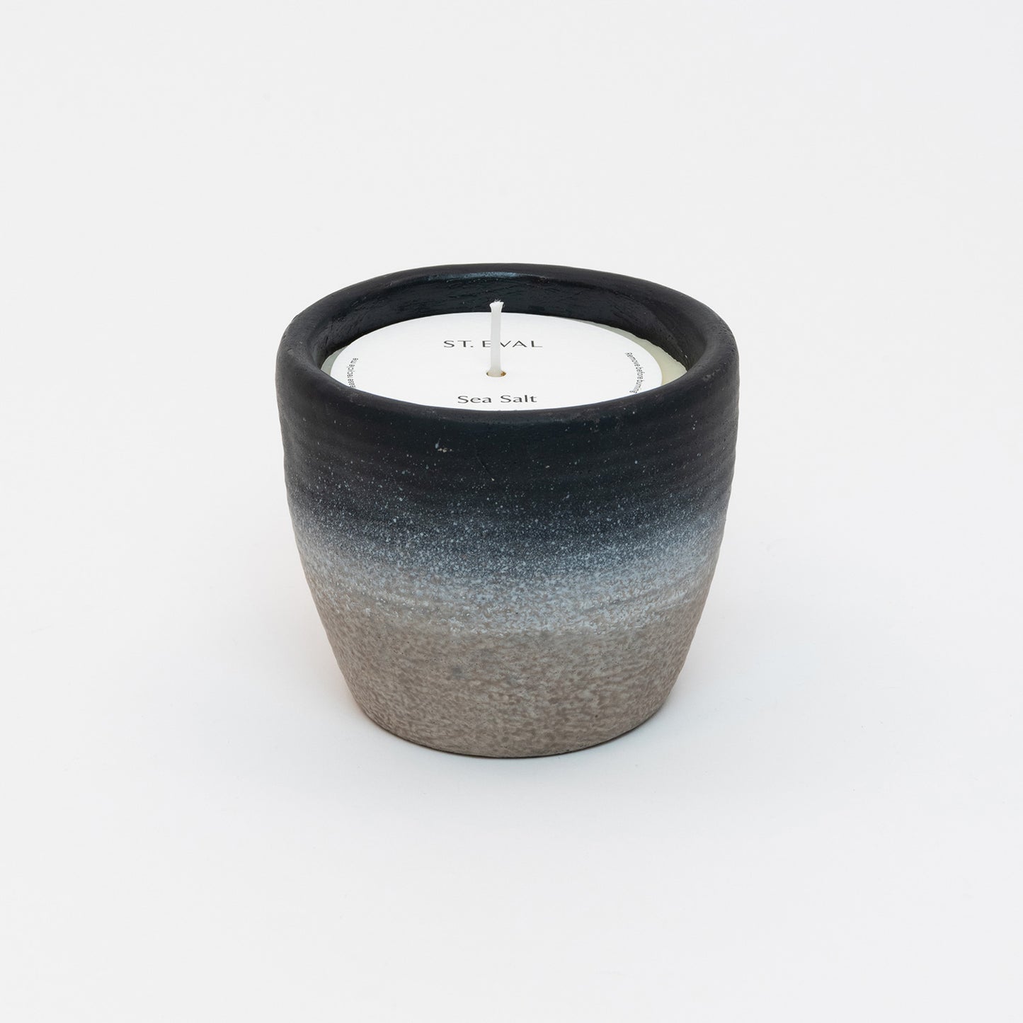 St Eval Sea Salt Large Coastal Candle in heavy stoneware pot. Natural stone clay base fading into a deep navy blue ring at top of pot. St Eval card circle protector on top of candle with wick standing tall.