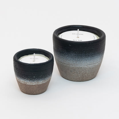 St Eval Sea Salt Small and Large Coastal Candle in heavy stoneware pot. Natural stone clay base fading into a deep navy blue ring at top of pot. St Eval card circle protector on top of candle with wick standing tall.