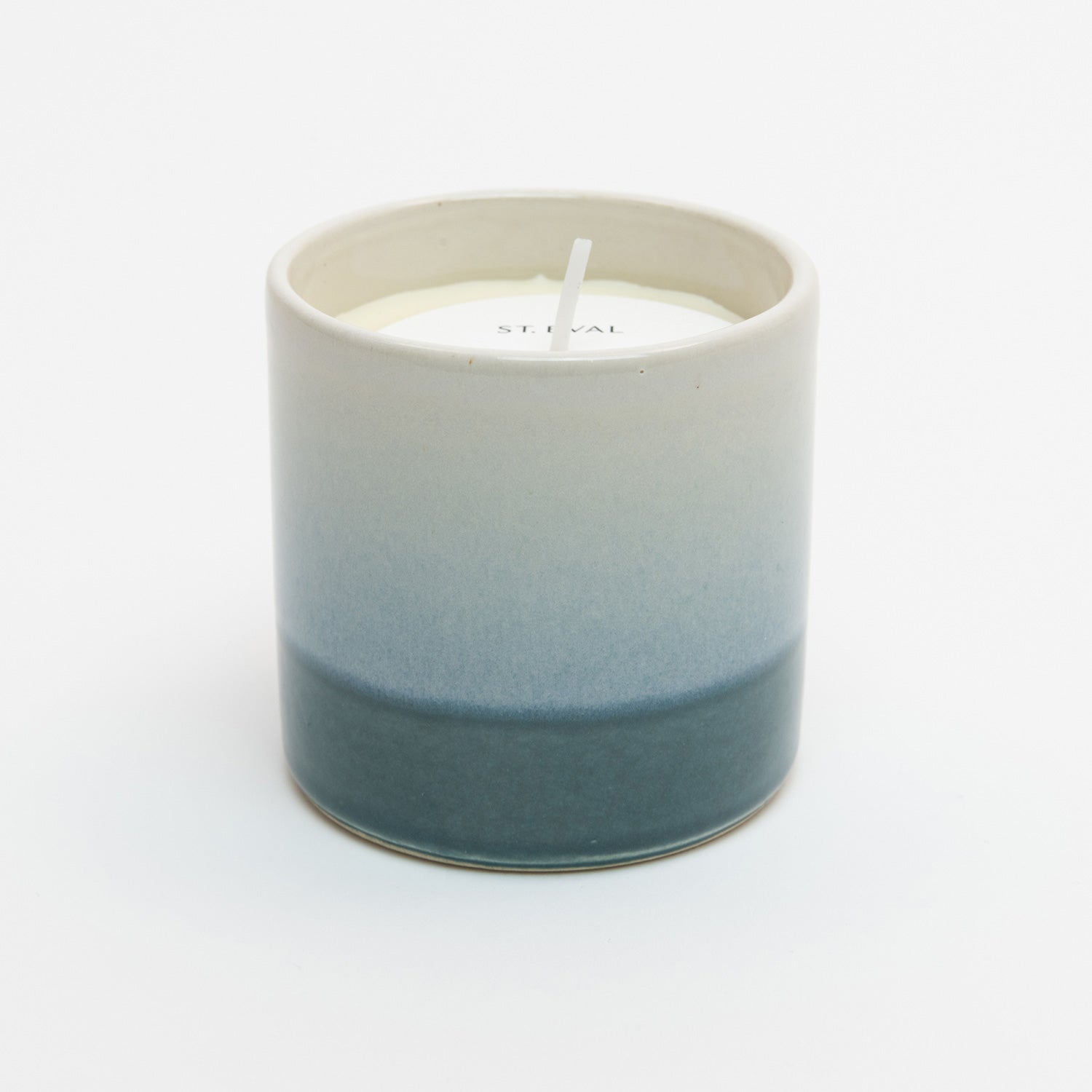 St Eval Sea & Shore Fig candle pot. Stoneware ceramic pot. Cream top fading to teal blue ring at base. St Eval card circle protector on top of candle with wick standing tall.
