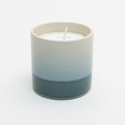 St Eval Sea & Shore Fig candle pot. Stoneware ceramic pot. Cream top fading to teal blue ring at base. St Eval card circle protector on top of candle with wick standing tall.