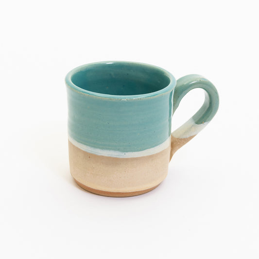 An espresso cup pictured on a white background. The cup has an ocean design, with the sea, a wave, and the sand across it.