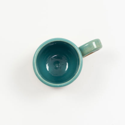 An espresso cup pictured on a white background. The cup has an ocean design, with the sea, a wave, and the sand across it.