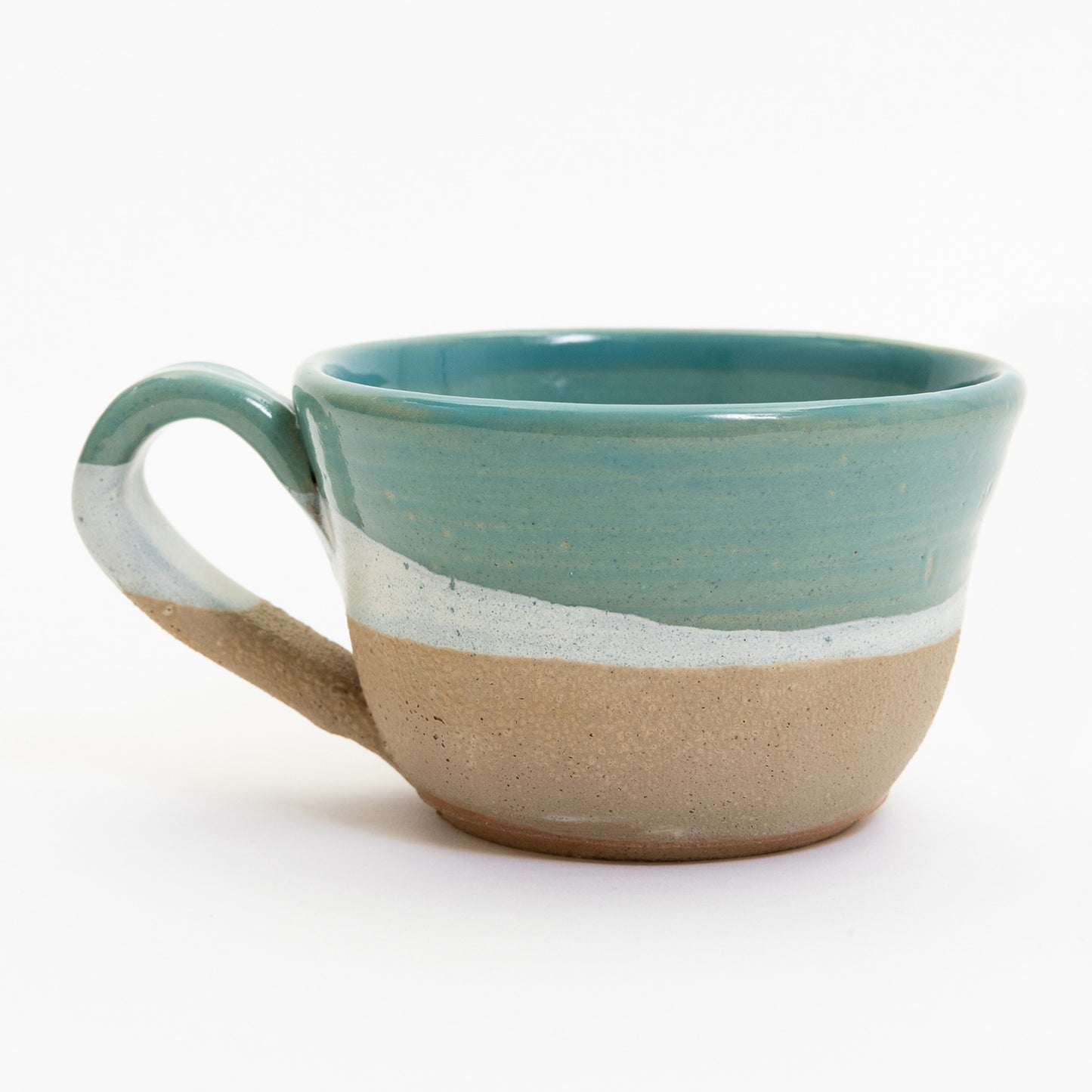 A mug featuring an ocean, wave, and shoreline design. Pictured on a white background.