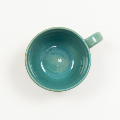 A mug featuring an ocean, wave, and shoreline design. Pictured on a white background.