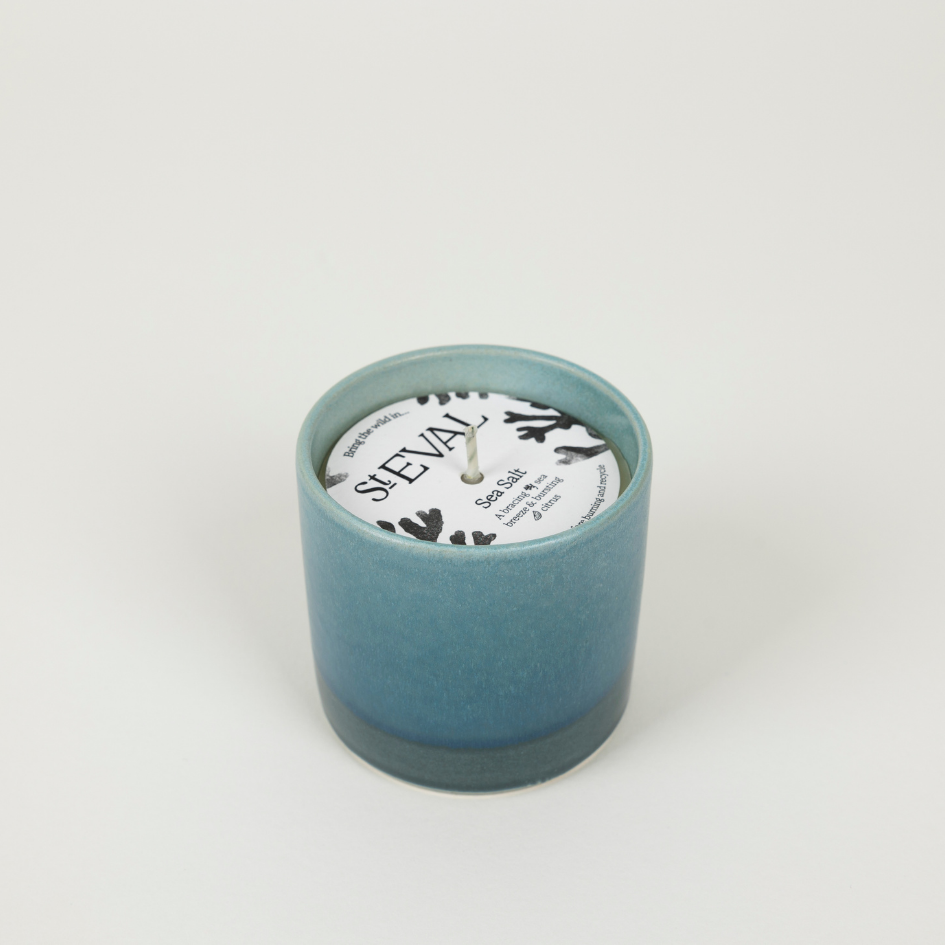 Teal candle in a textured container with a white label on a light grey background
