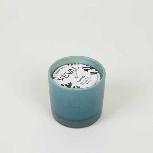 Teal candle in a textured container with a white label on a light grey background
