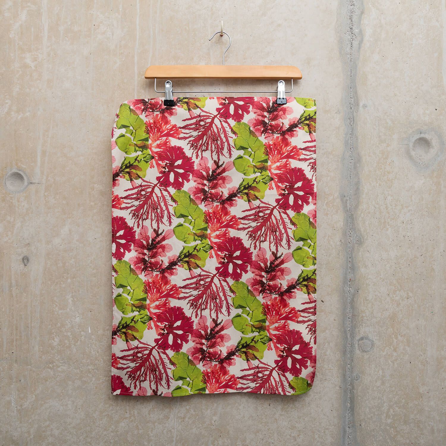 Wooden hanger holding a tea towel showing pressed seaweeds in pinks and greens