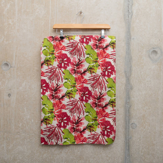 Wooden hanger holding a tea towel showing pressed seaweeds in pinks and greens