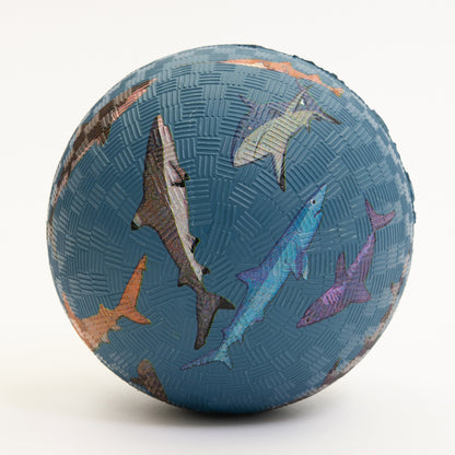 A blue rubber ball with shark designs on it. Pictured on a white background.