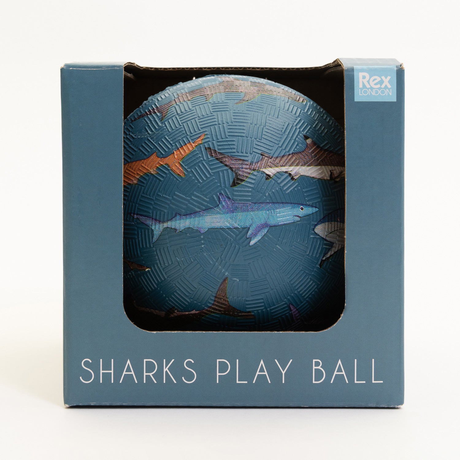 A blue rubber ball with shark designs on it. Pictured in a blue cardboard box on a white background.