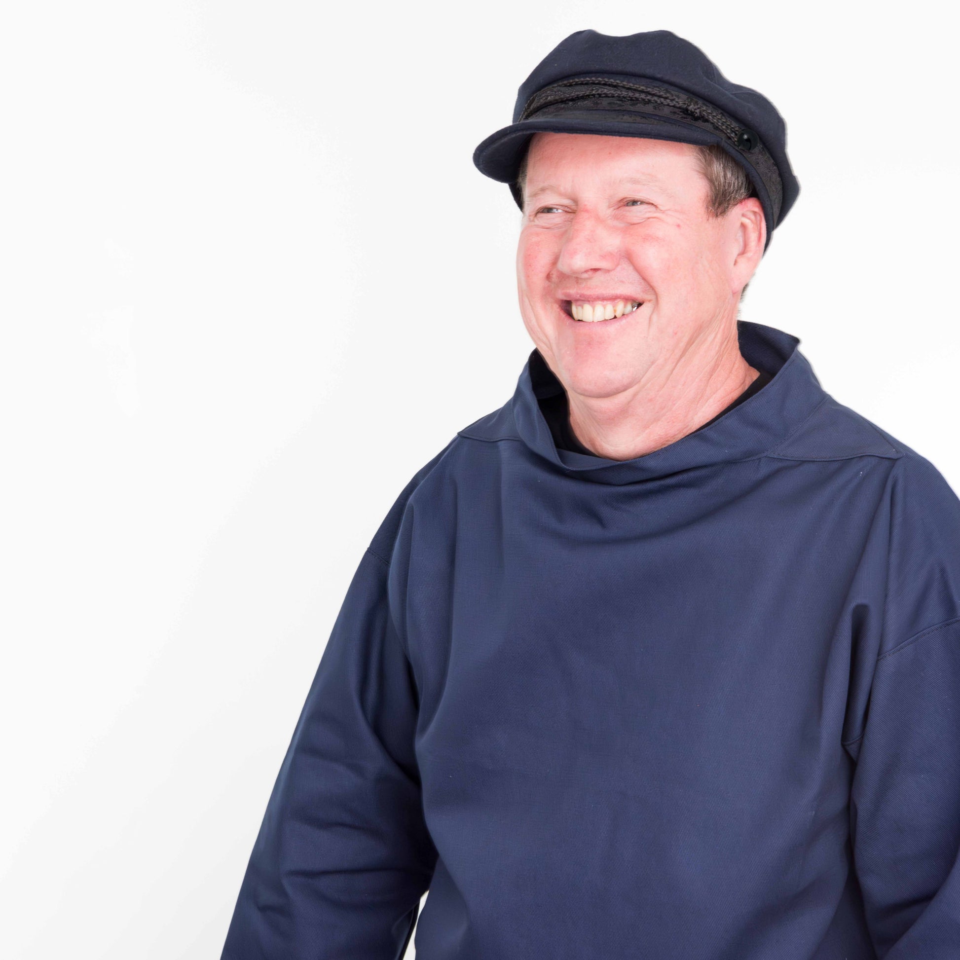 Man wearing a navy smock and a navy Breton cap on white background
