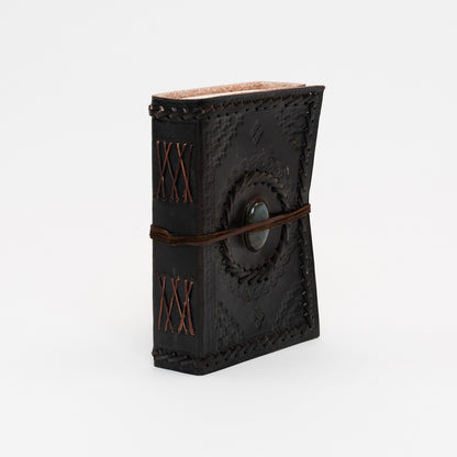 A dark brown leather bound journal with stitching on the spine and a stone on the cover.