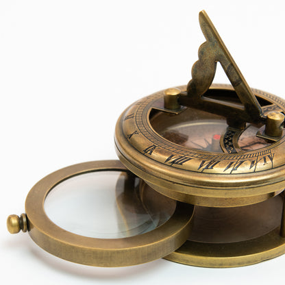 A brass sundial, compass and magnifier chart weight pictured on a white background.