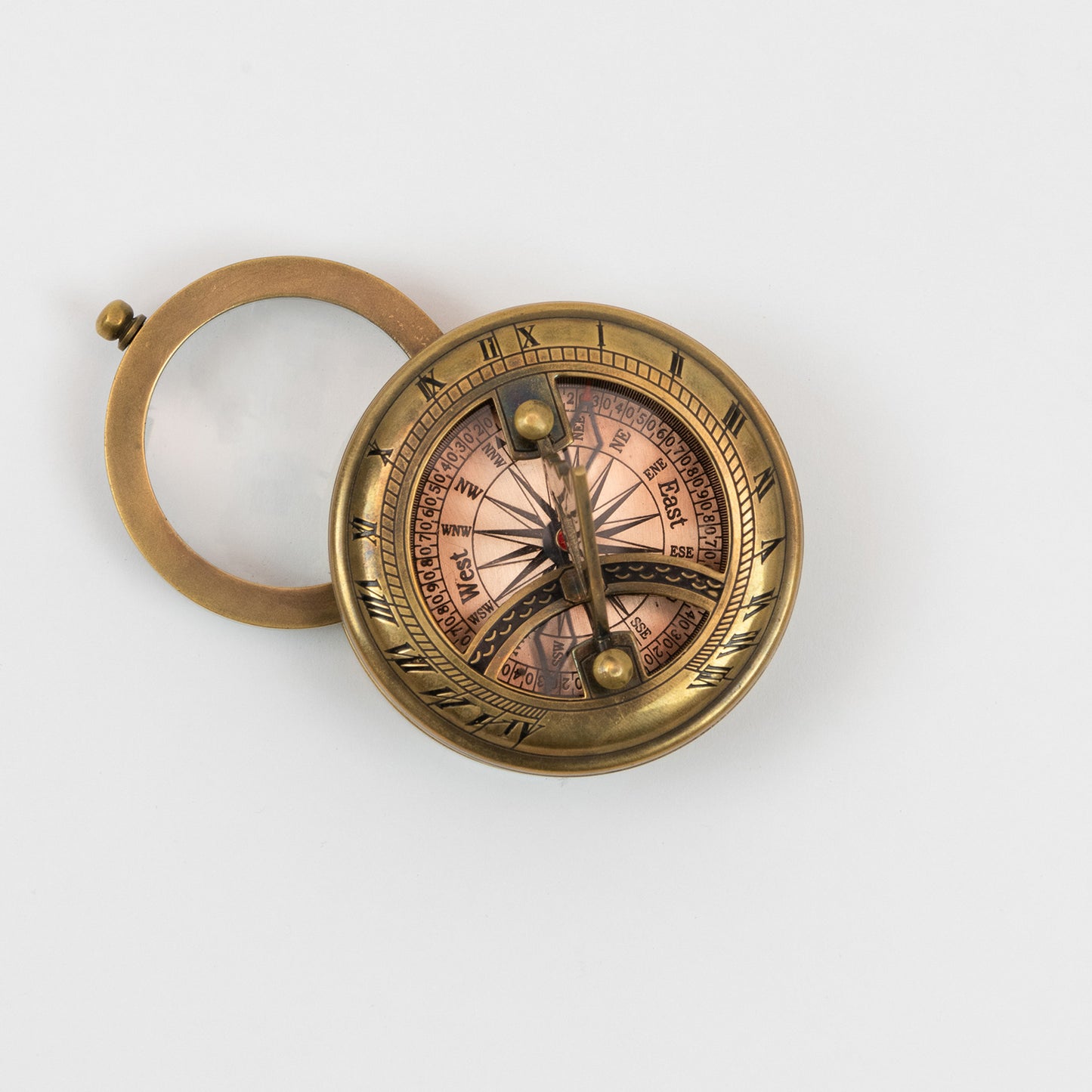 A brass sundial, compass and magnifier chart weight pictured on a white background.