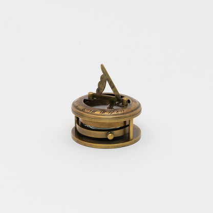 A brass sundial, compass and magnifier chart weight pictured on a white background.