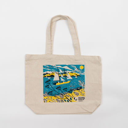 The Falmouth Tall Ship Tote Bag featuring a blue, yellow and white design of a tall ship in full sail. The tote bag is laid flat against a white background.