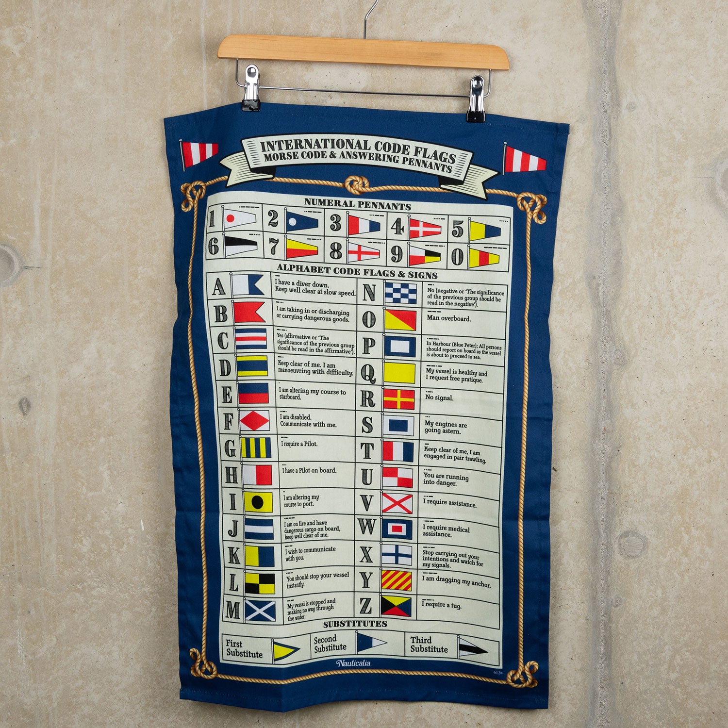 Multi-coloured international Code Flags tea towel with flags for each letter of the alphabet and for numbers 0 to 9. The tea towel is hanging from a hanger on a grey background.