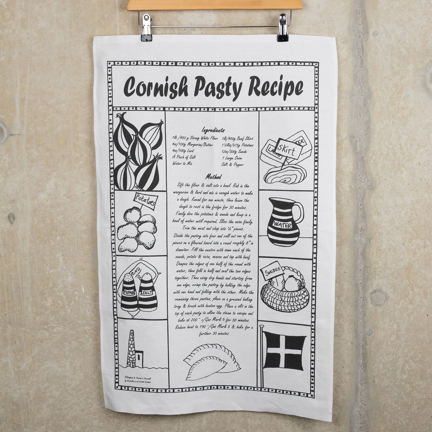 Black and white Cornish pasty recipe tea towel hanging from a hanger against a grey background.