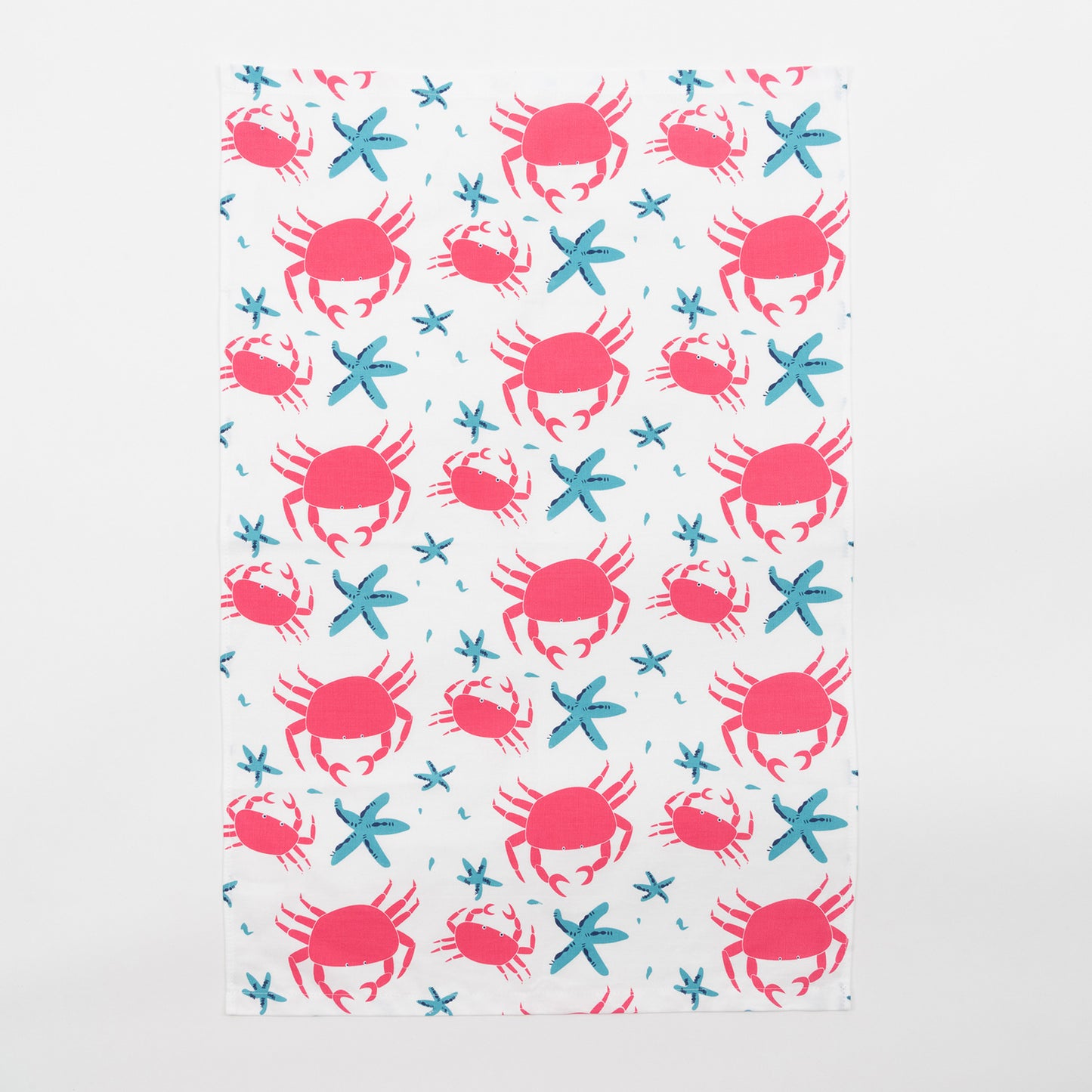 The crab and starfish tea towel features pink crabs and blue starfish on a light cream background. The tea towel is against a white background.