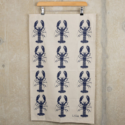 Navy lobster repeated pattern on a cream coloured tea towel. The Navy Lobster Tea Towel is hanging from a clip hanger against a grey background.